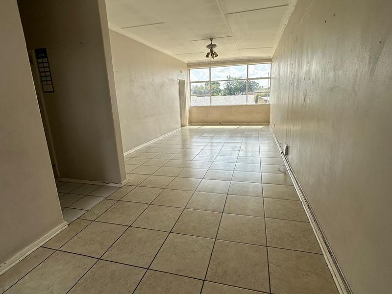 An empty, open-plan living area featuring neutral tiled flooring, a ceiling fan, and large windows providing natural light.