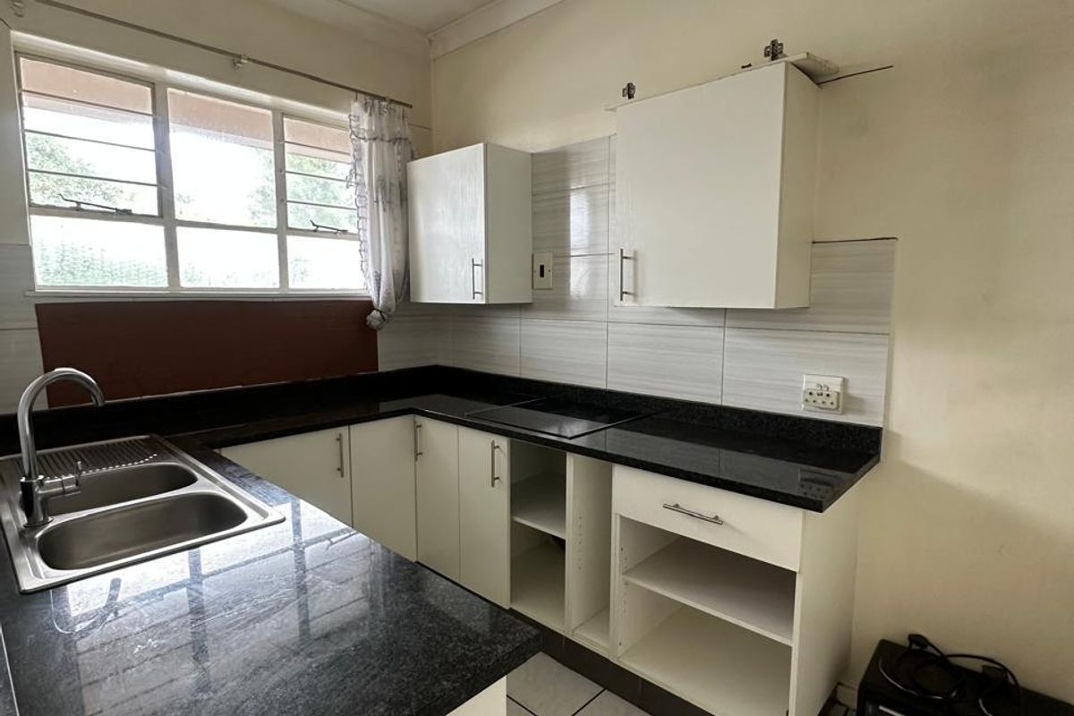 A compact kitchen featuring granite countertops, double basin sink, and tiled flooring. The space requires minor repairs to cabinetry and finishes.