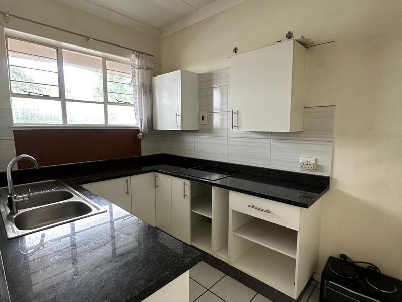 A compact kitchen featuring granite countertops, double basin sink, and tiled flooring. The space requires minor repairs to cabinetry and finishes.
