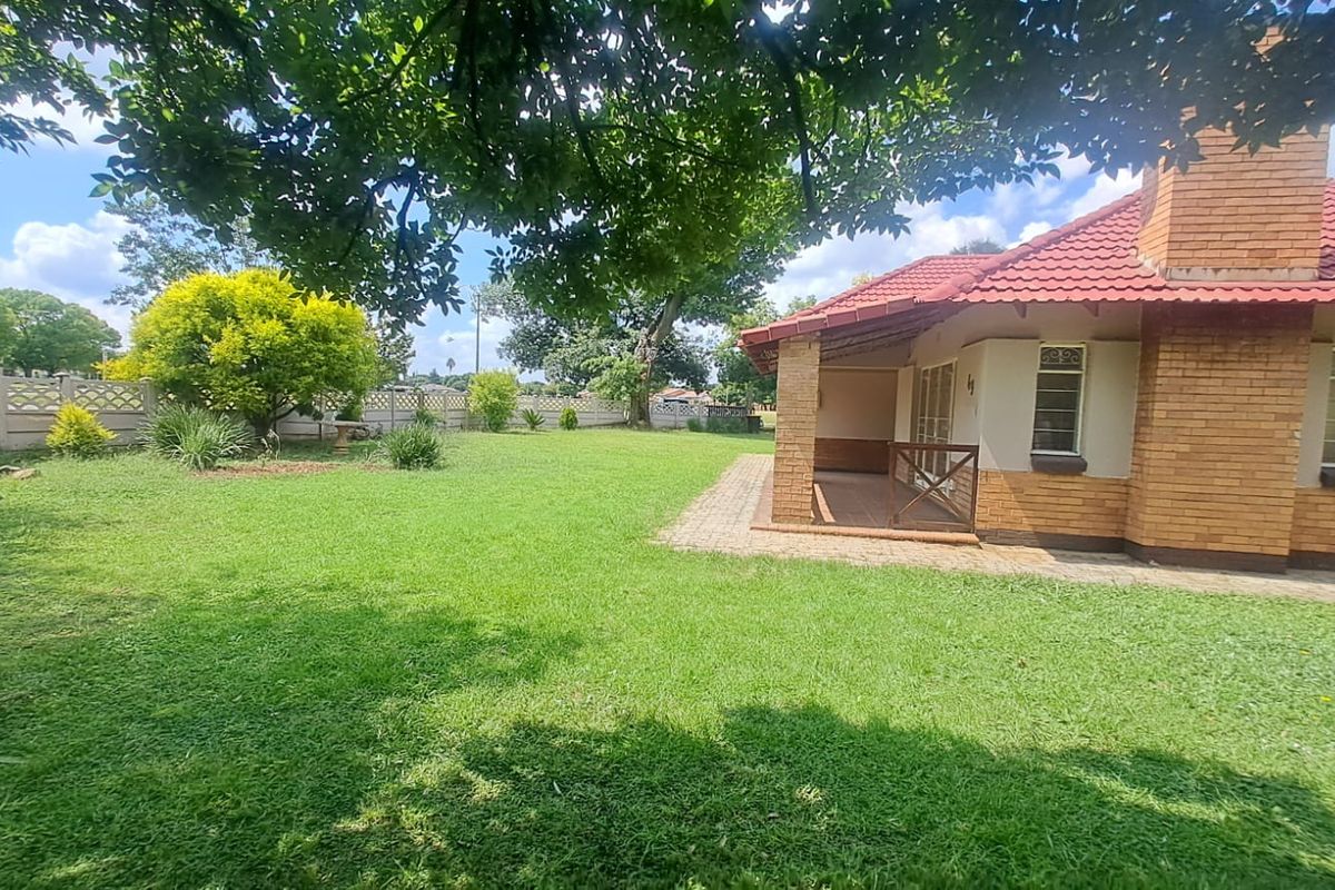 Spacious rear garden featuring a well-maintained lawn, mature trees, and a covered brick patio area attached to the main house.