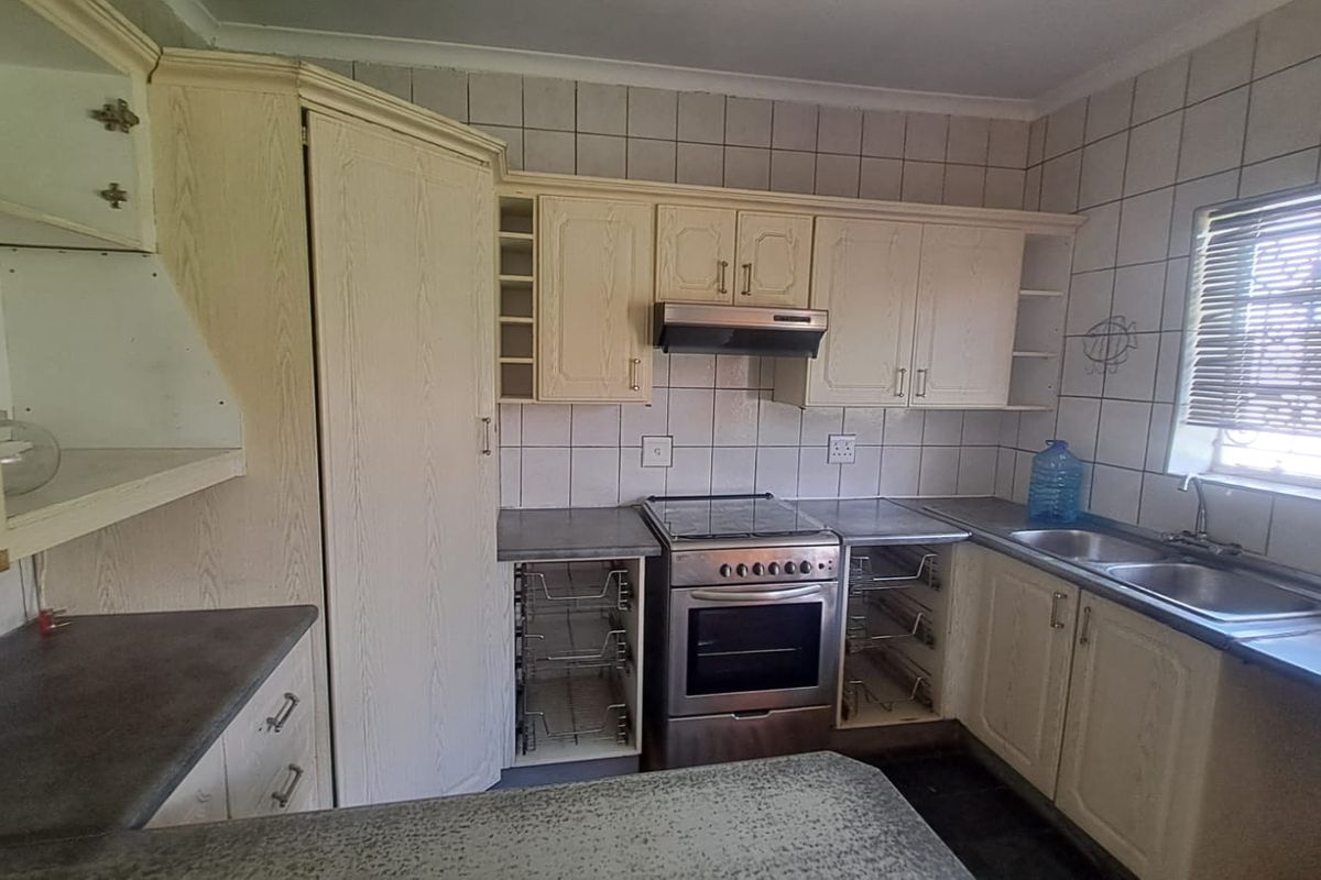 A functional kitchen featuring built-in cabinetry, a stainless steel stove with extractor fan, double basin sink, and tiled backsplash.