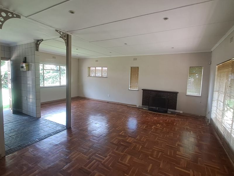 Spacious open-plan living area featuring classic parquet flooring, a brick fireplace, and a distinct tiled entryway with decorative archway detailing.