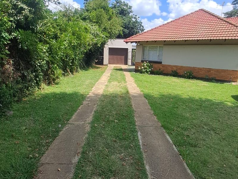 A view of the front exterior featuring a concrete driveway leading to a garage, with a tiled roof house and surrounding lawn.