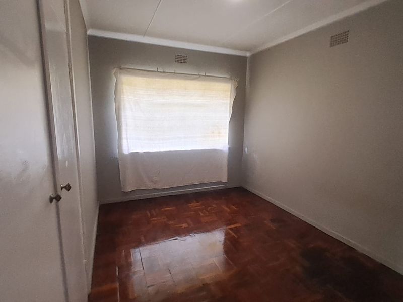 An empty bedroom featuring original parquet flooring, a built-in cupboard, and neutral wall finishes, offering a blank canvas for renovation.