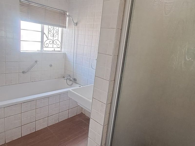A dated bathroom featuring a built-in bathtub, separate shower enclosure, and full-height wall tiling. The space is vacant and ready for renovation.