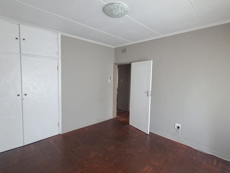 A vacant bedroom featuring original parquet flooring, built-in cupboards, and neutral wall tones, offering a blank canvas for personalization.