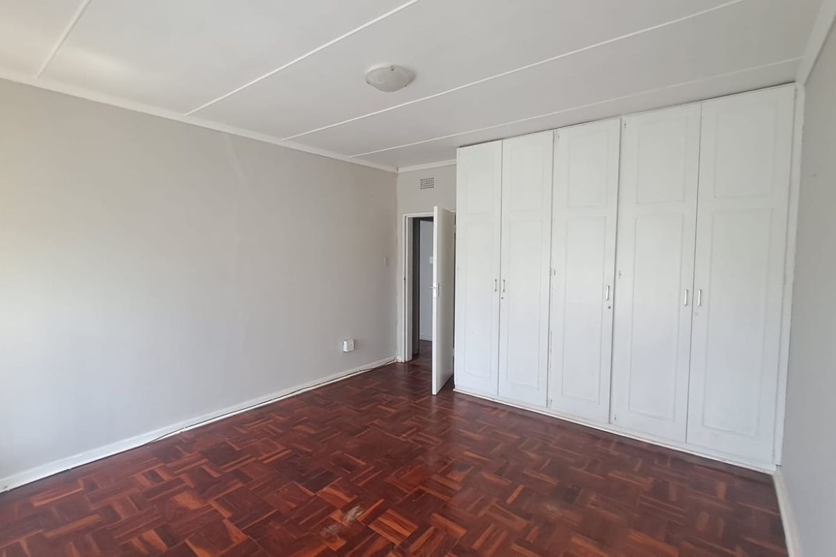 A spacious, empty bedroom featuring classic parquet flooring and extensive built-in white cupboards, offering a clean and neutral canvas for personalization.