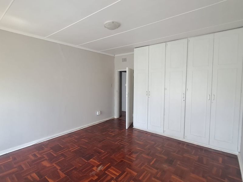 A spacious, empty bedroom featuring classic parquet flooring and extensive built-in white cupboards, offering a clean and neutral canvas for personalization.