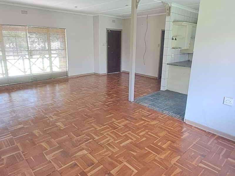 Spacious open-plan living area featuring classic parquet flooring, recessed lighting, and an adjoining kitchen space with built-in cabinetry.