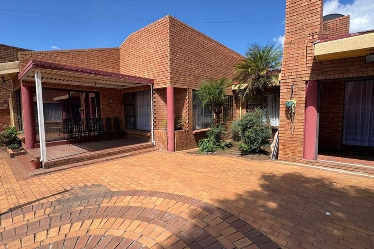 Rear exterior view featuring a spacious brick-paved courtyard, covered patio area, and traditional brick architecture with sliding door access to the home.
