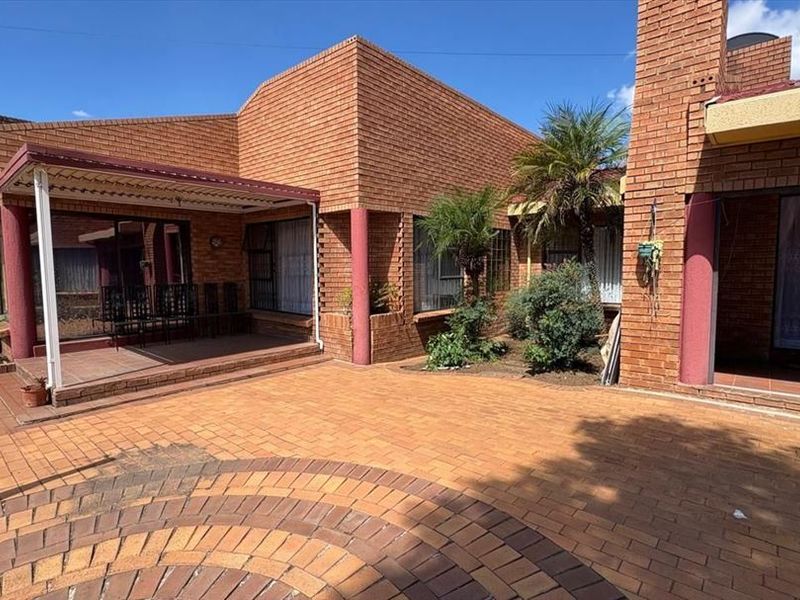 Rear exterior view featuring a spacious brick-paved courtyard, covered patio area, and traditional brick architecture with sliding door access to the home.
