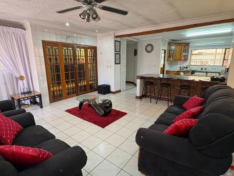 Open plan living area featuring tiled floors, a breakfast bar with brick detailing, and a kitchen with wooden cabinetry.