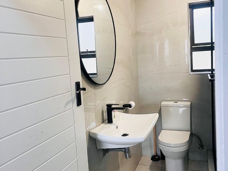 A modern, compact bathroom featuring neutral wall tiles, a wall-mounted basin with black fixtures, and a sleek toilet.