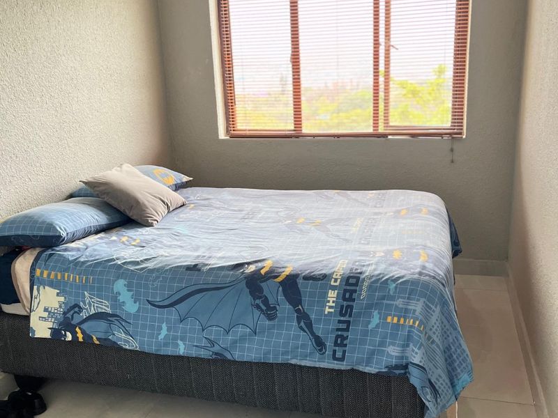 A bedroom featuring tiled flooring, textured walls, and a window fitted with horizontal blinds.