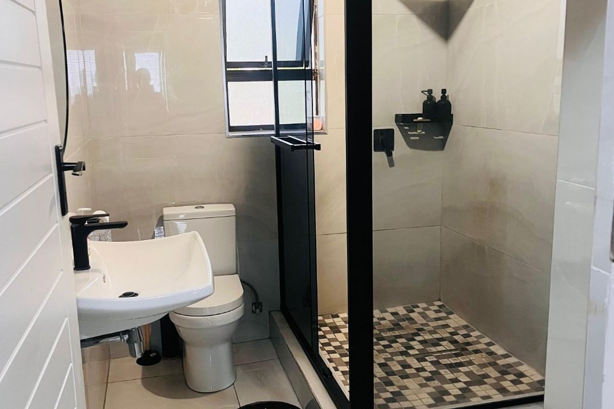 Modern bathroom featuring a walk-in shower with black frame, wall-mounted basin, and tiled finishes.