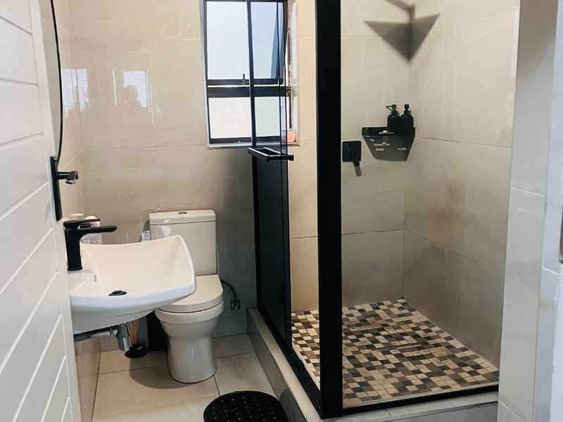 Modern bathroom featuring a walk-in shower with black frame, wall-mounted basin, and tiled finishes.