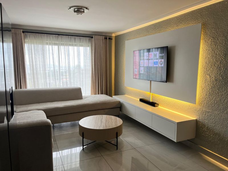 A modern living room featuring a built-in media console, textured accent wall with integrated LED lighting, and large windows with sheer curtains.