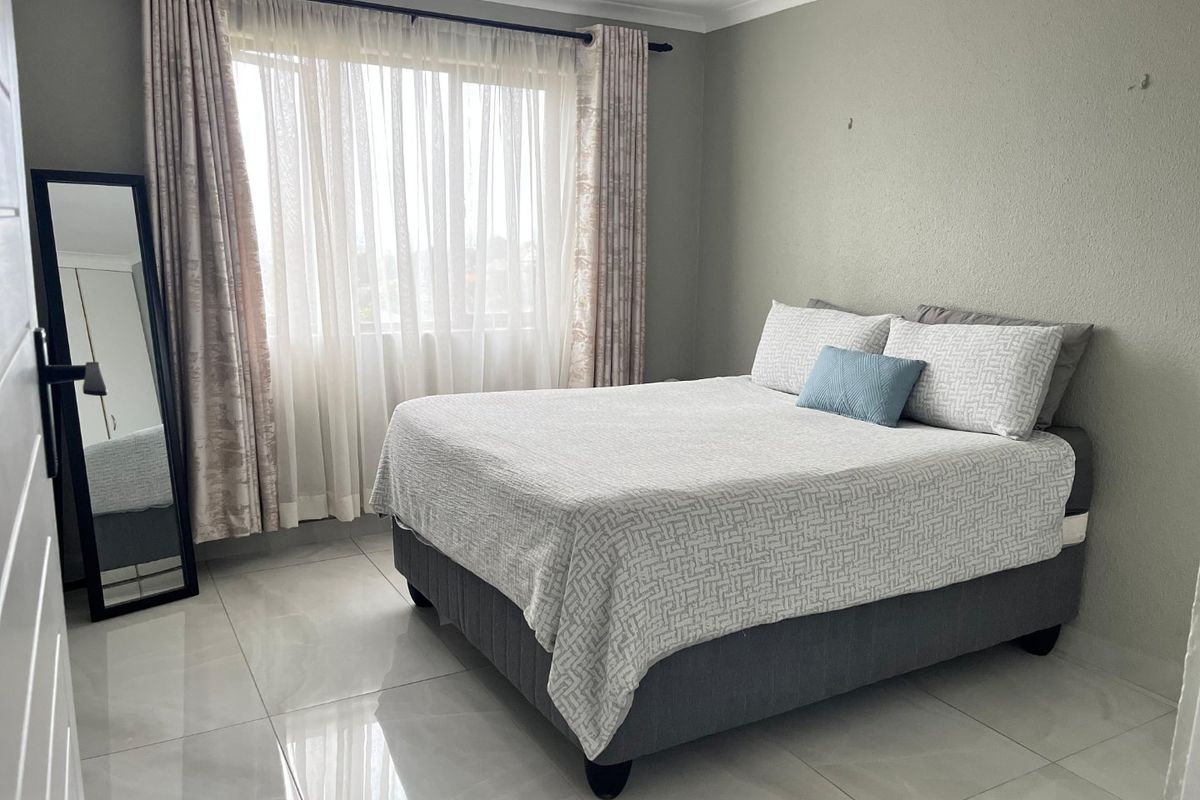 A well-lit bedroom featuring large format floor tiles, neutral wall finishes, and a window with curtain tracks.