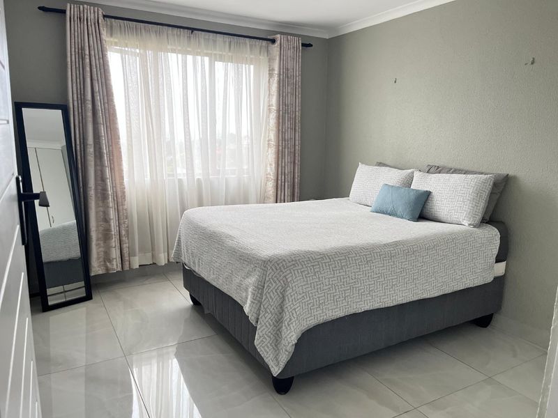 A well-lit bedroom featuring large format floor tiles, neutral wall finishes, and a window with curtain tracks.