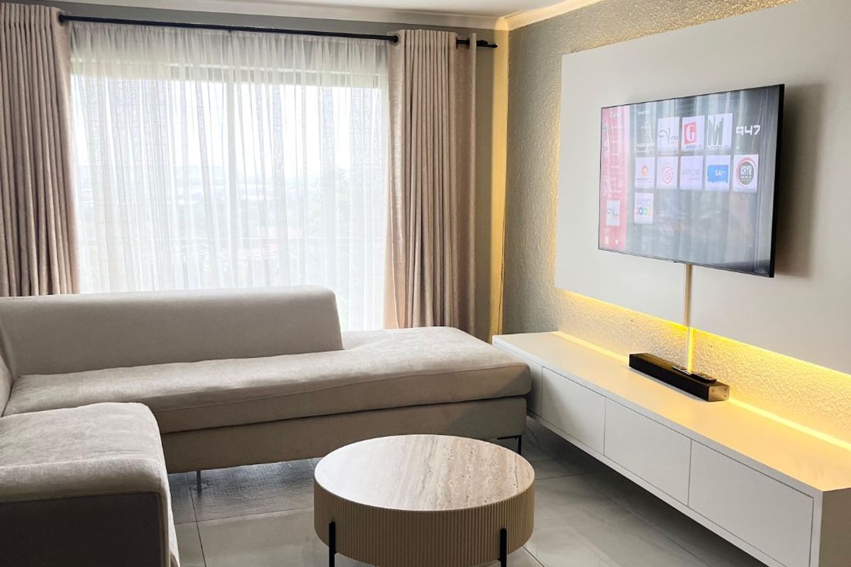 Modern living room featuring a custom built-in media wall with integrated LED accent lighting, large format floor tiles, and floor-to-ceiling window treatments.