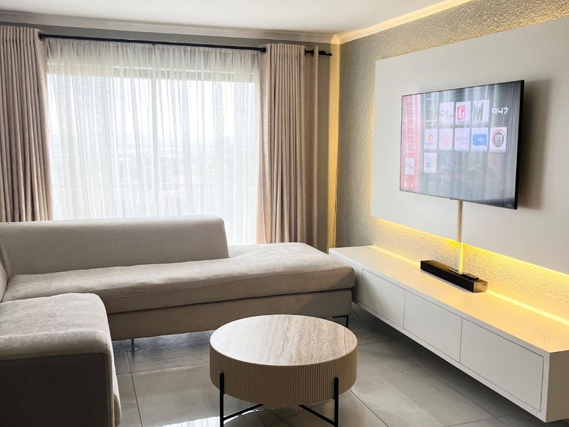 Modern living room featuring a custom built-in media wall with integrated LED accent lighting, large format floor tiles, and floor-to-ceiling window treatments.