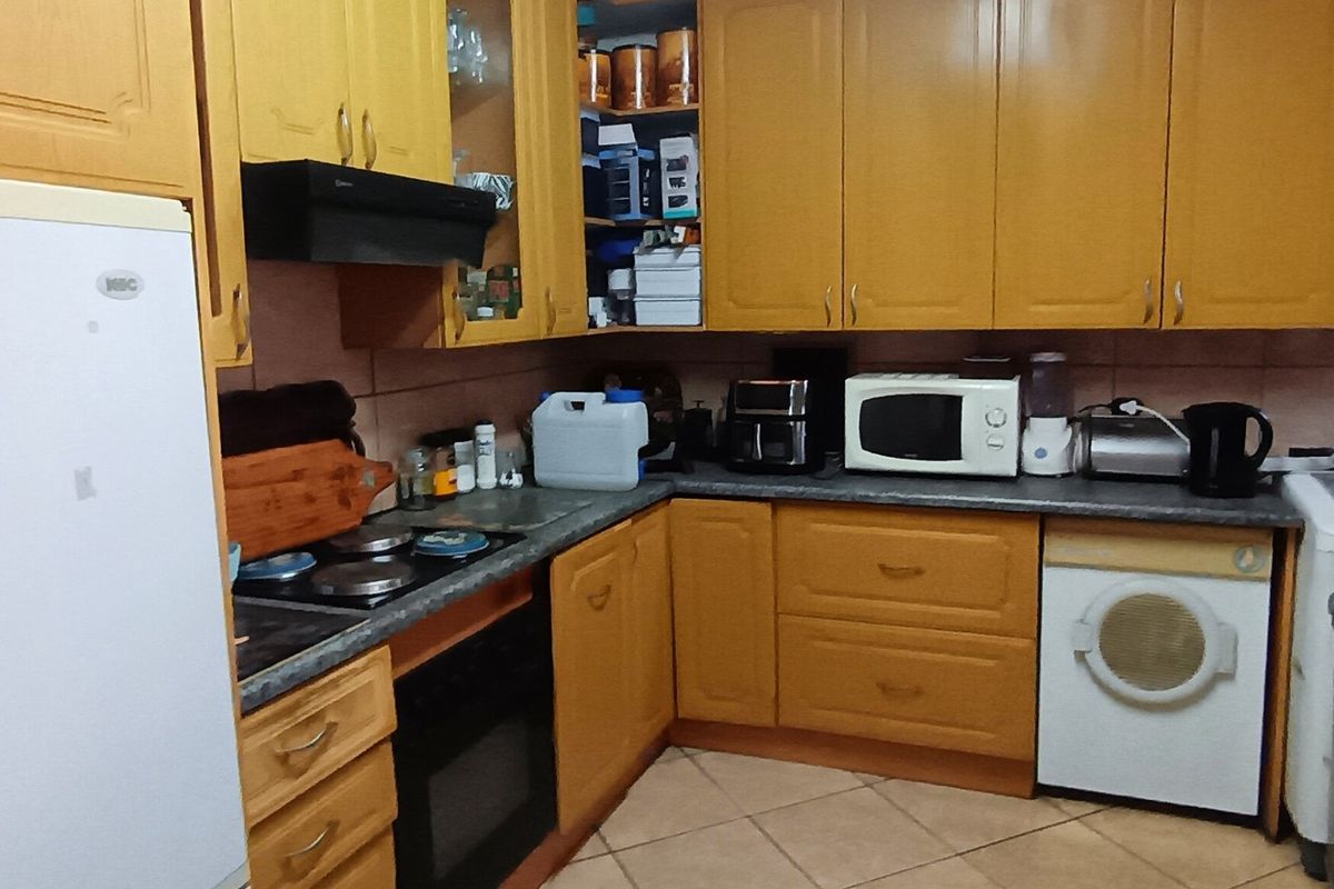 A functional kitchen featuring wooden cabinetry, tiled backsplash, and integrated appliances, offering a practical layout with potential for modern updates.