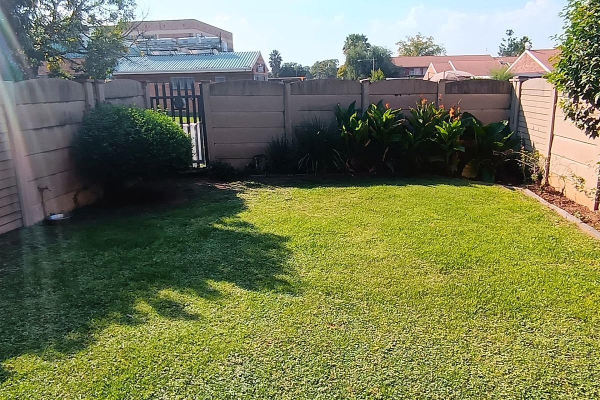 A private rear garden featuring a well-maintained lawn enclosed by precast concrete boundary walls and a secure metal pedestrian gate.