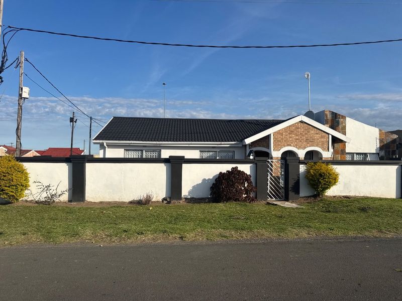 Front view of a single-story house featuring a tiled roof, brick accents, and a secure perimeter wall with a gated entrance.