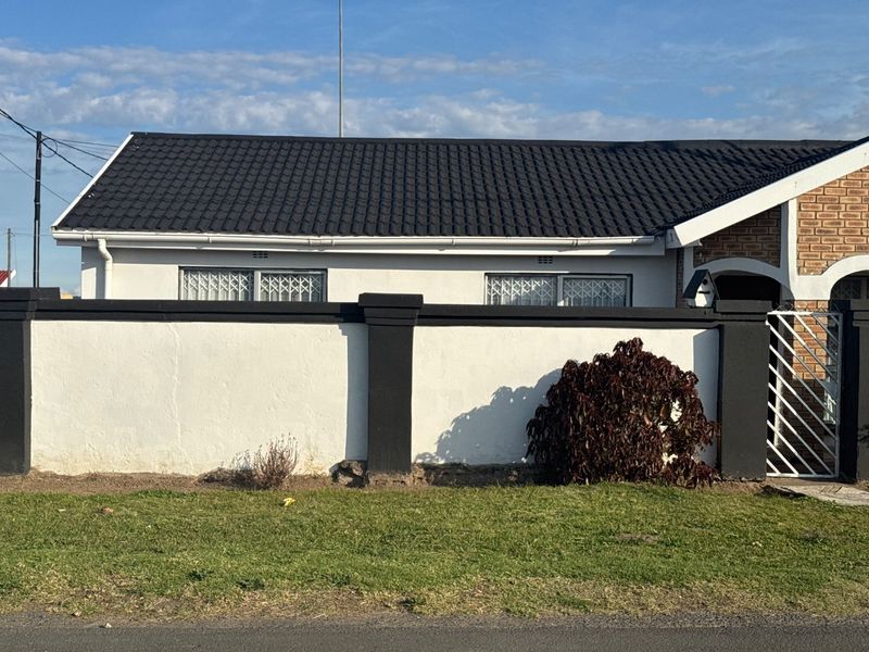 Front view of a residential house featuring a tiled roof, white exterior walls, and a secure boundary wall with gated access.