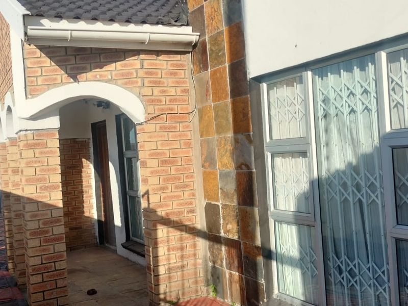 Front exterior view of the house featuring a brick facade, stone cladding accents, an arched entrance, and security gates on the windows.