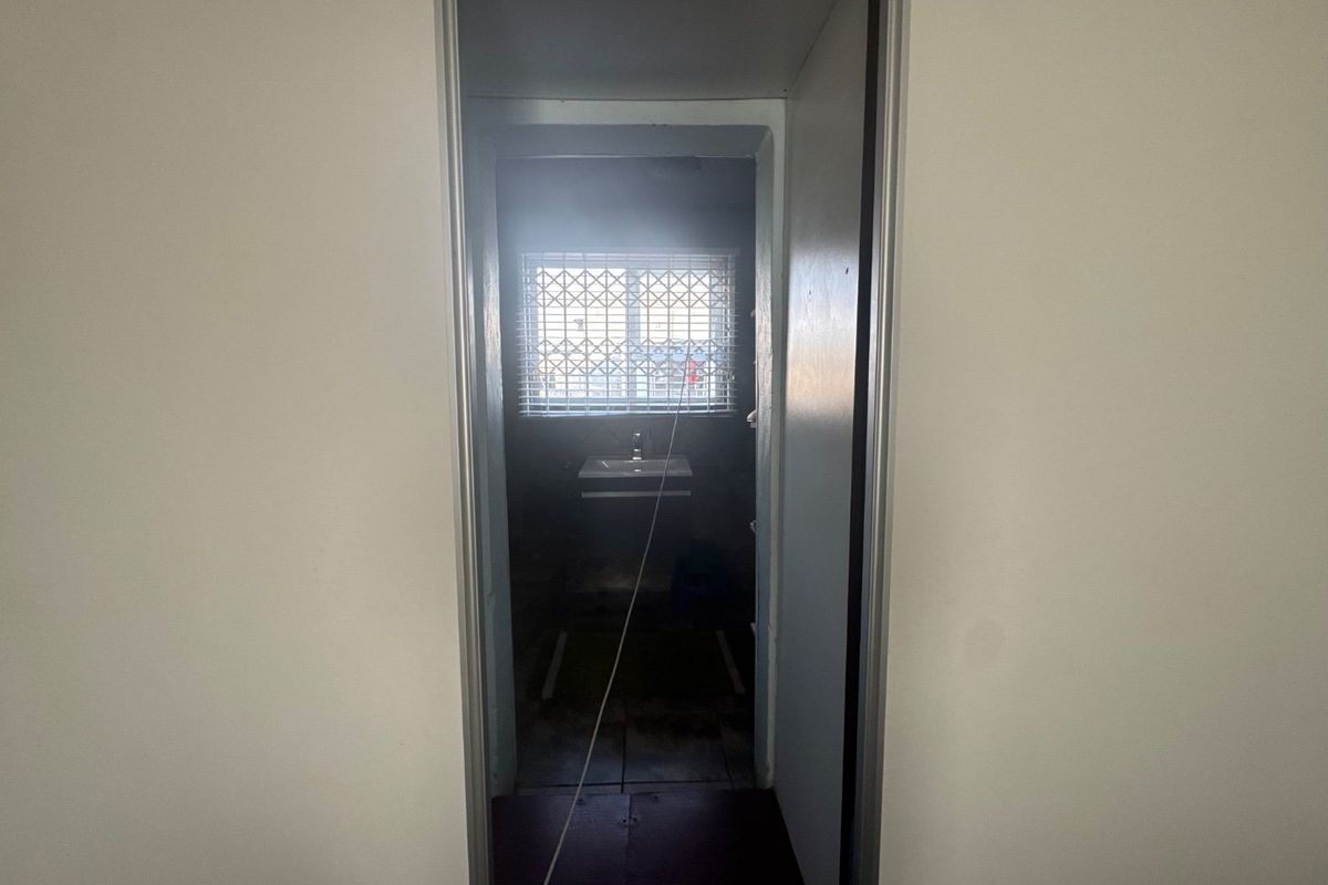 A view into a small, dimly lit bathroom featuring a wall-mounted basin and tiled flooring, currently in need of cosmetic updates.