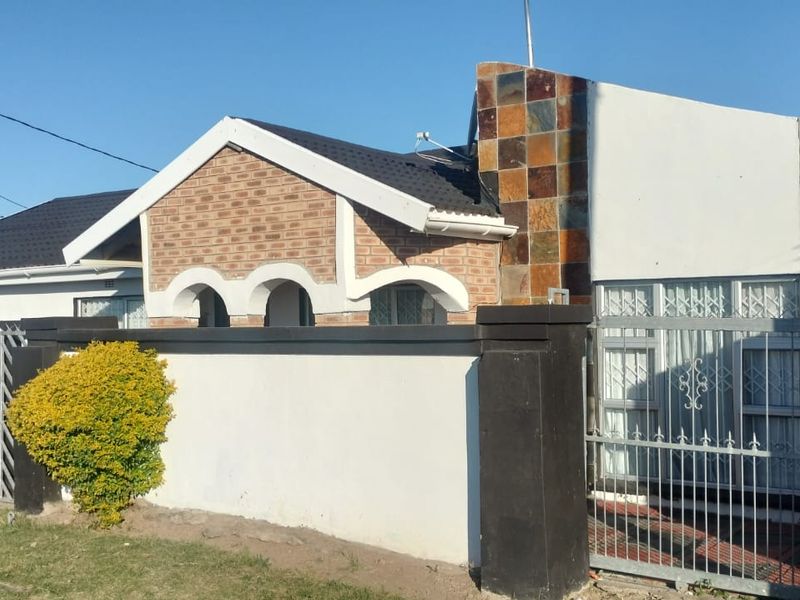 Front elevation of a residential house featuring a brick facade, stone cladding accents, a tiled roof, and a secure perimeter wall with a metal gate.