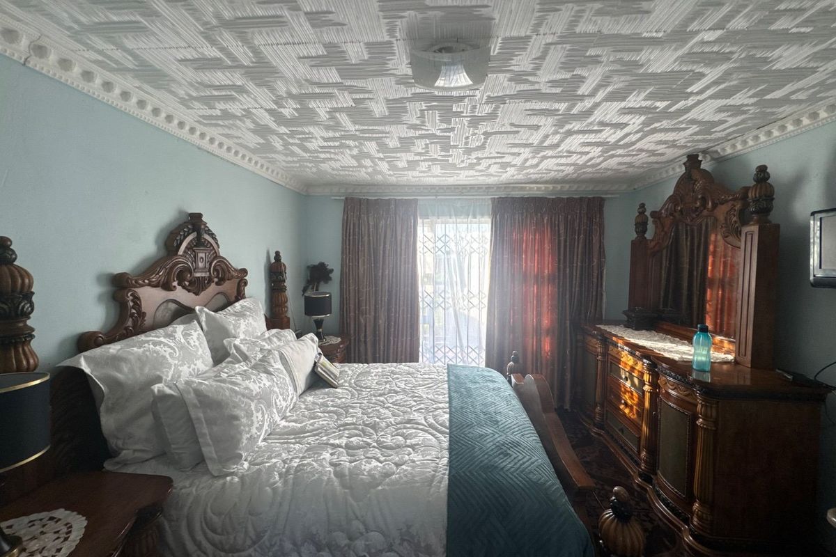 A spacious bedroom featuring a distinctive textured ceiling with decorative cornicing and access to an outdoor area through a security gate.