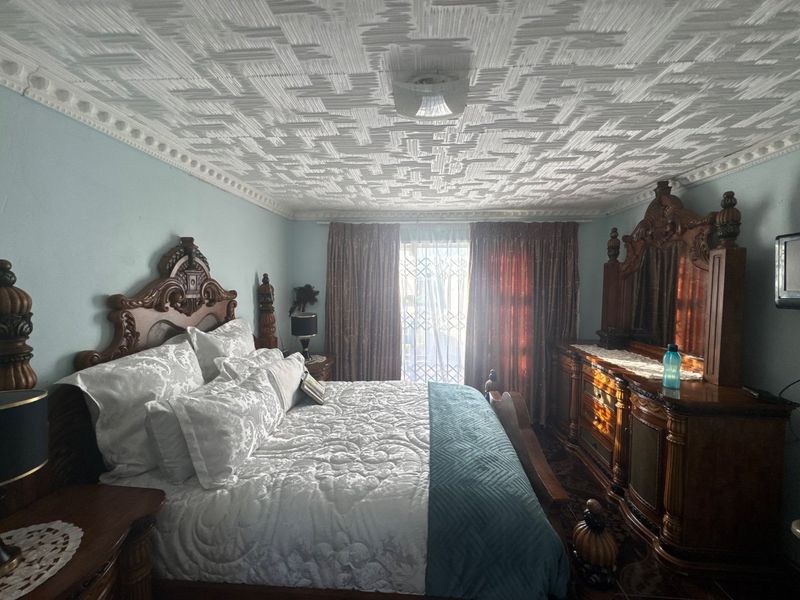 A spacious bedroom featuring a distinctive textured ceiling with decorative cornicing and access to an outdoor area through a security gate.