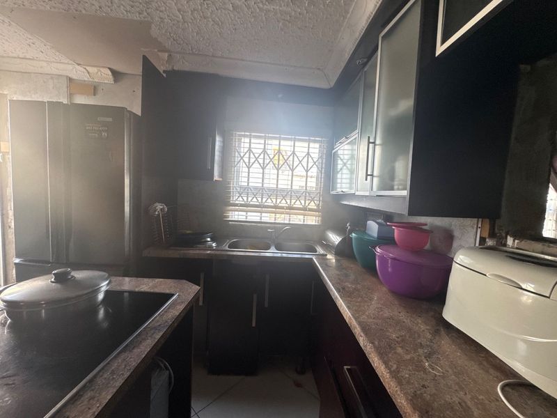 A compact kitchen featuring dark cabinetry, laminate countertops, and a double bowl sink, requiring ceiling repairs and cosmetic updates to modernize the space.