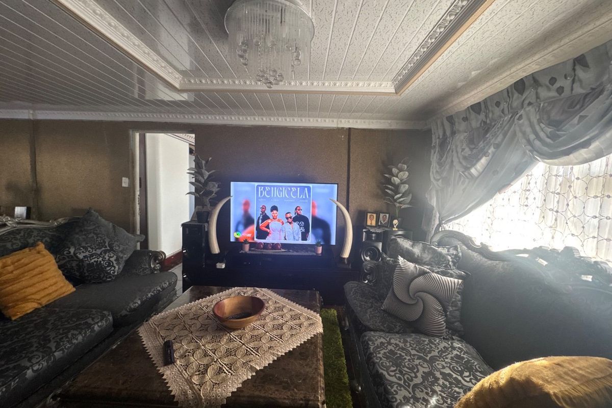 A living room featuring decorative ceiling panels, crown molding, and a central chandelier, providing a traditional aesthetic.