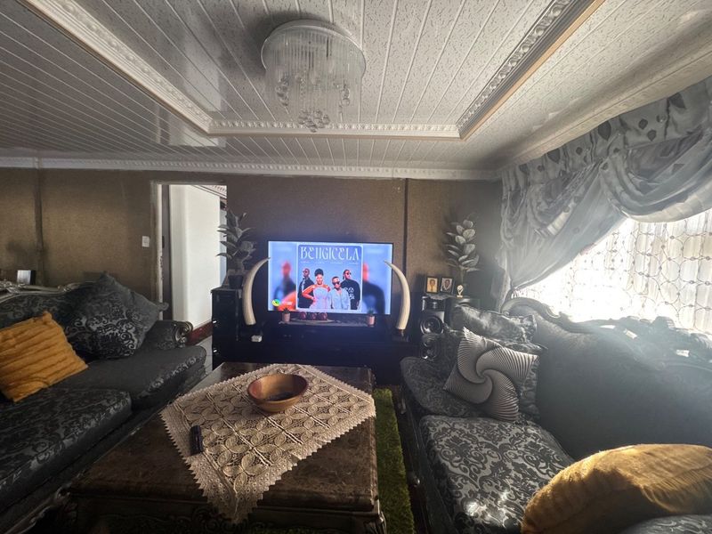 A living room featuring decorative ceiling panels, crown molding, and a central chandelier, providing a traditional aesthetic.