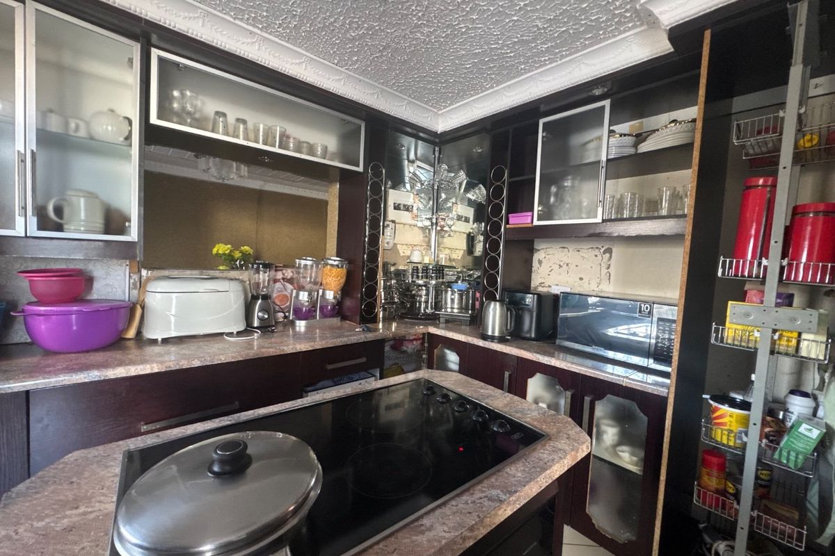 A dated kitchen featuring dark cabinetry, laminate countertops, and an integrated electric cooktop with decorative ceiling detailing.