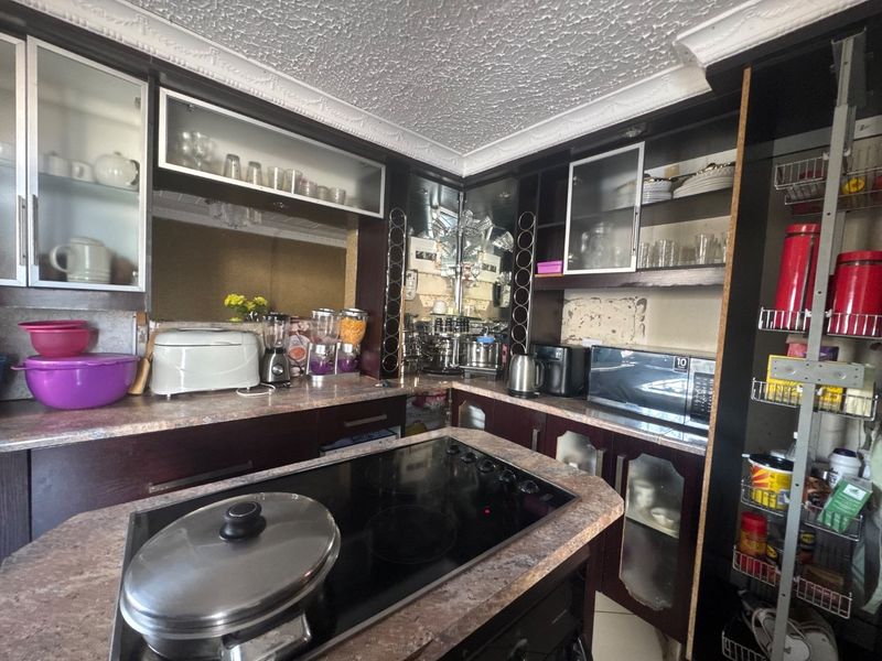 A dated kitchen featuring dark cabinetry, laminate countertops, and an integrated electric cooktop with decorative ceiling detailing.