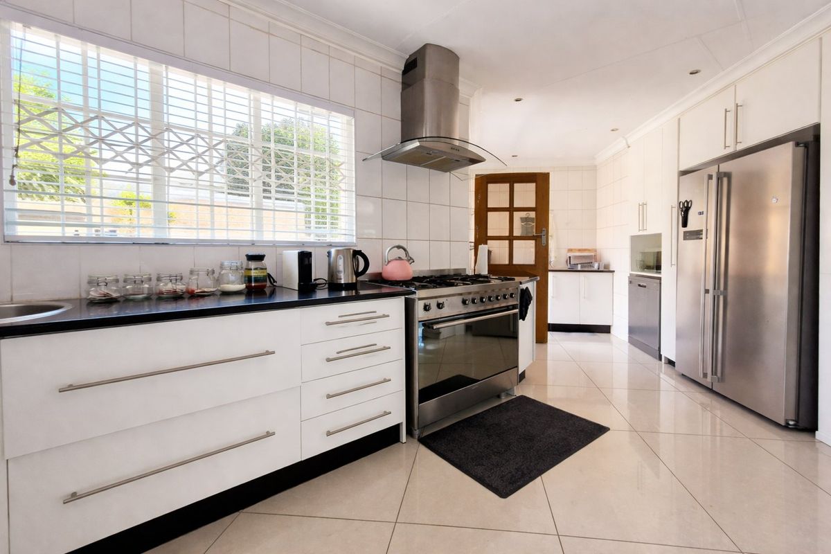 A functional kitchen featuring white cabinetry, a gas stove with stainless steel extractor fan, tiled flooring, and a large window with security bars.