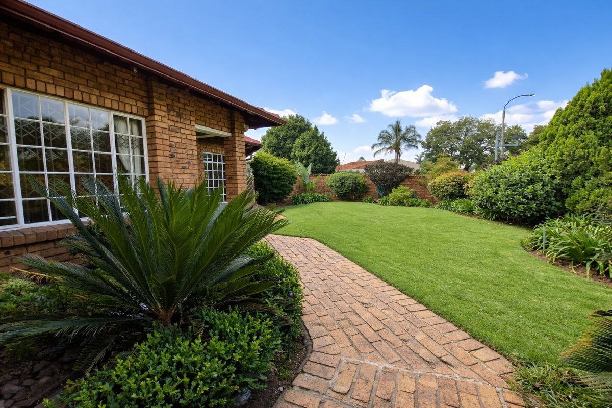 A well-maintained rear garden featuring a brick-paved pathway, lush green lawn, and established perimeter landscaping alongside the brick house exterior.