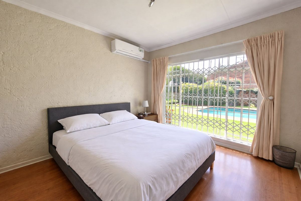 A bedroom featuring laminate flooring, a wall-mounted air conditioning unit, and a sliding glass door with a security gate overlooking the pool area.