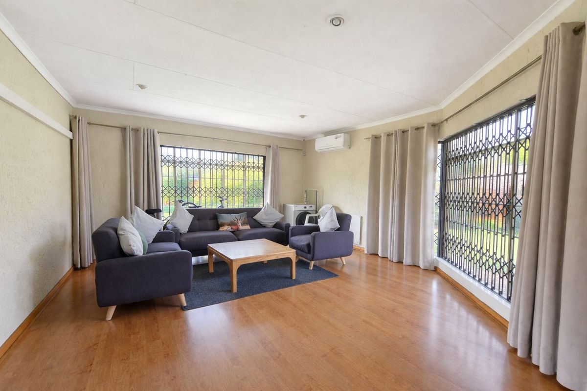 Spacious living room featuring laminate flooring, recessed lighting, and security gates on windows, equipped with a wall-mounted air conditioning unit.