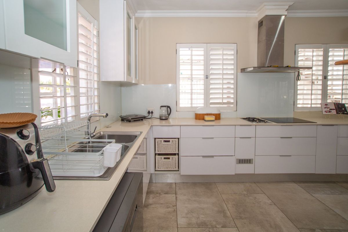 A modern, well-maintained kitchen featuring white cabinetry, stone countertops, a stainless steel extractor fan, and plantation shutters for natural light.
