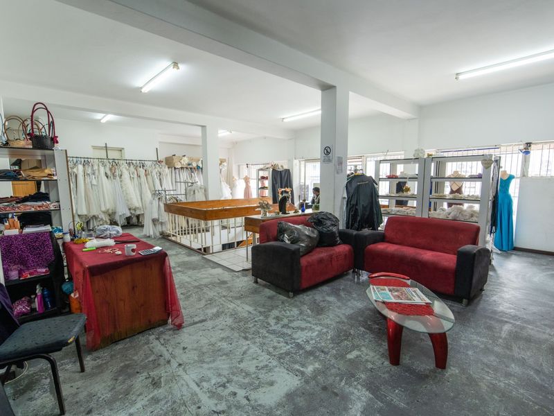 Open-plan commercial space featuring concrete flooring, fluorescent lighting, and security window bars, currently utilized as a retail showroom.