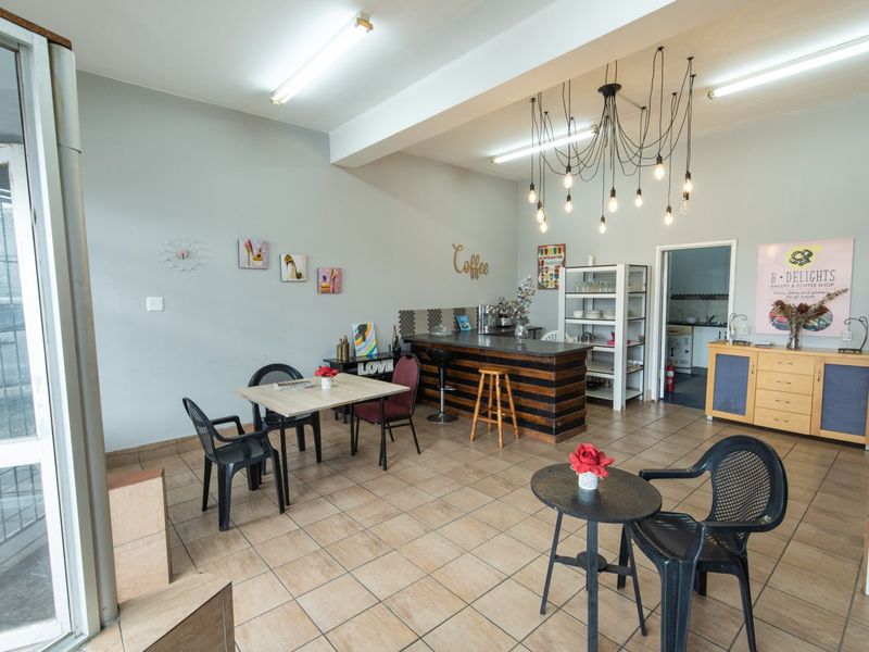 Open-plan commercial space featuring tiled flooring, a built-in service counter with tiled backsplash, and a mix of fluorescent and decorative pendant lighting.