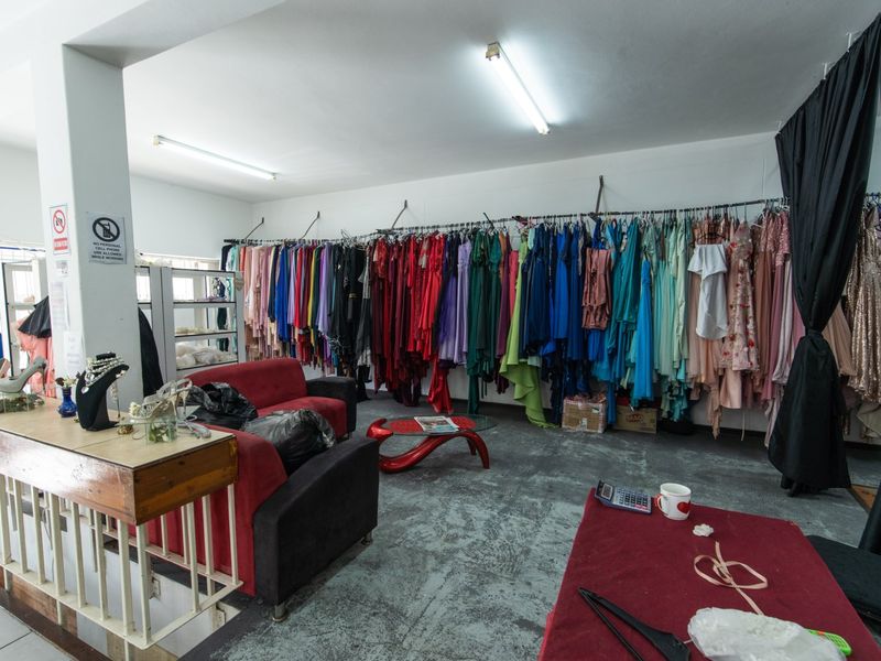 A commercial retail space featuring wall-mounted clothing rails, fluorescent lighting, and industrial concrete flooring, currently utilized as a clothing boutique.