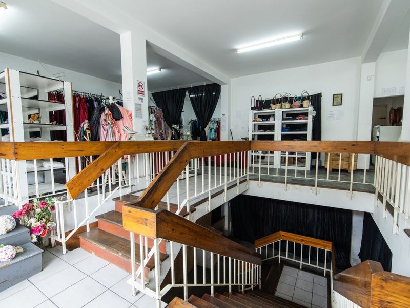 A multi-level commercial space featuring a central staircase with wooden handrails, tiled flooring, and open-plan layout suitable for retail or showroom use.