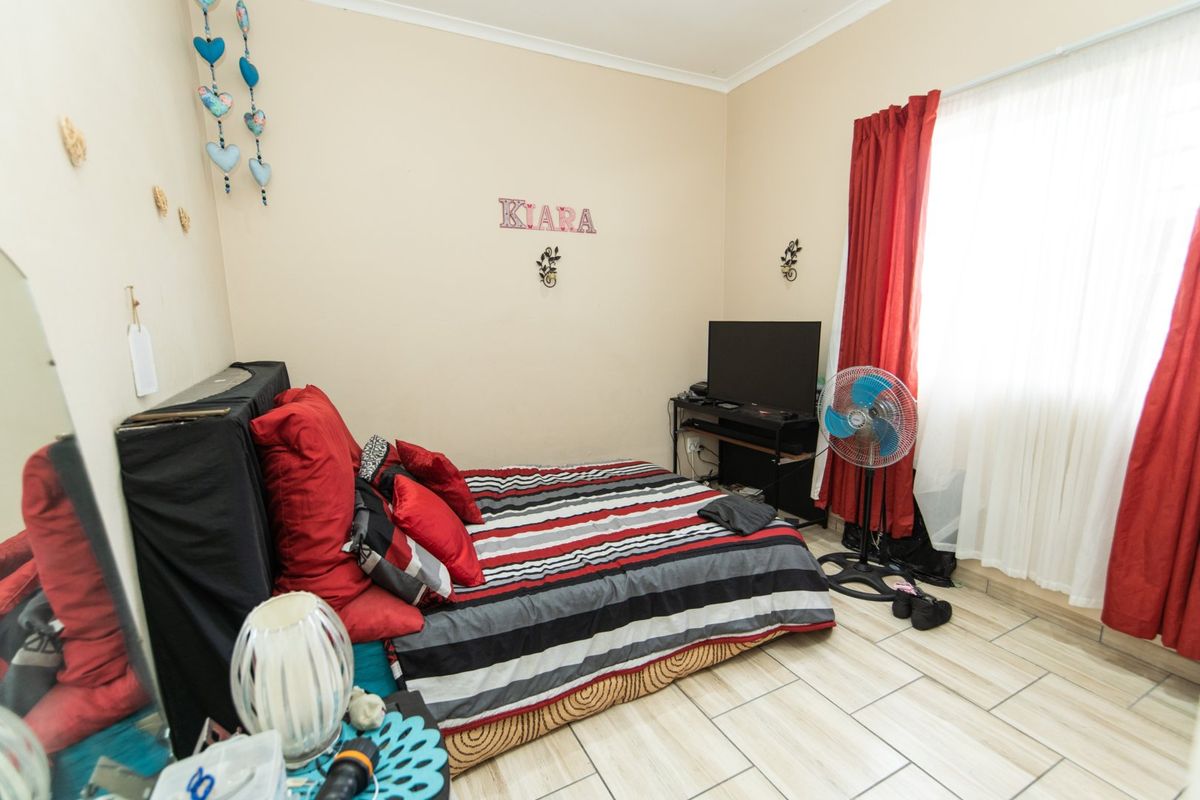A standard bedroom featuring tiled flooring and natural light from a window with installed curtain rails.