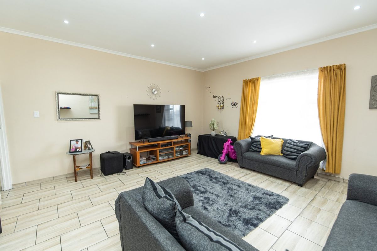 A spacious living room featuring neutral wall tones, ceramic tiled flooring, and recessed downlighting, providing a comfortable and well-lit area for relaxation.